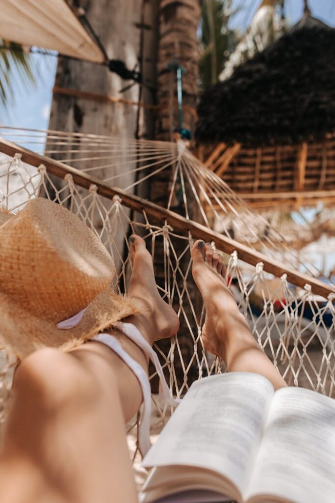 A tranquil summer day, reading and relaxing in a hammock, legs up, with a straw hat for shade.